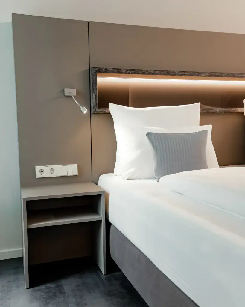 Doppelzimmer im Seehotel Tankumsee mit Doppelbett, grauem Kissen, Nachttisch und Leselampe