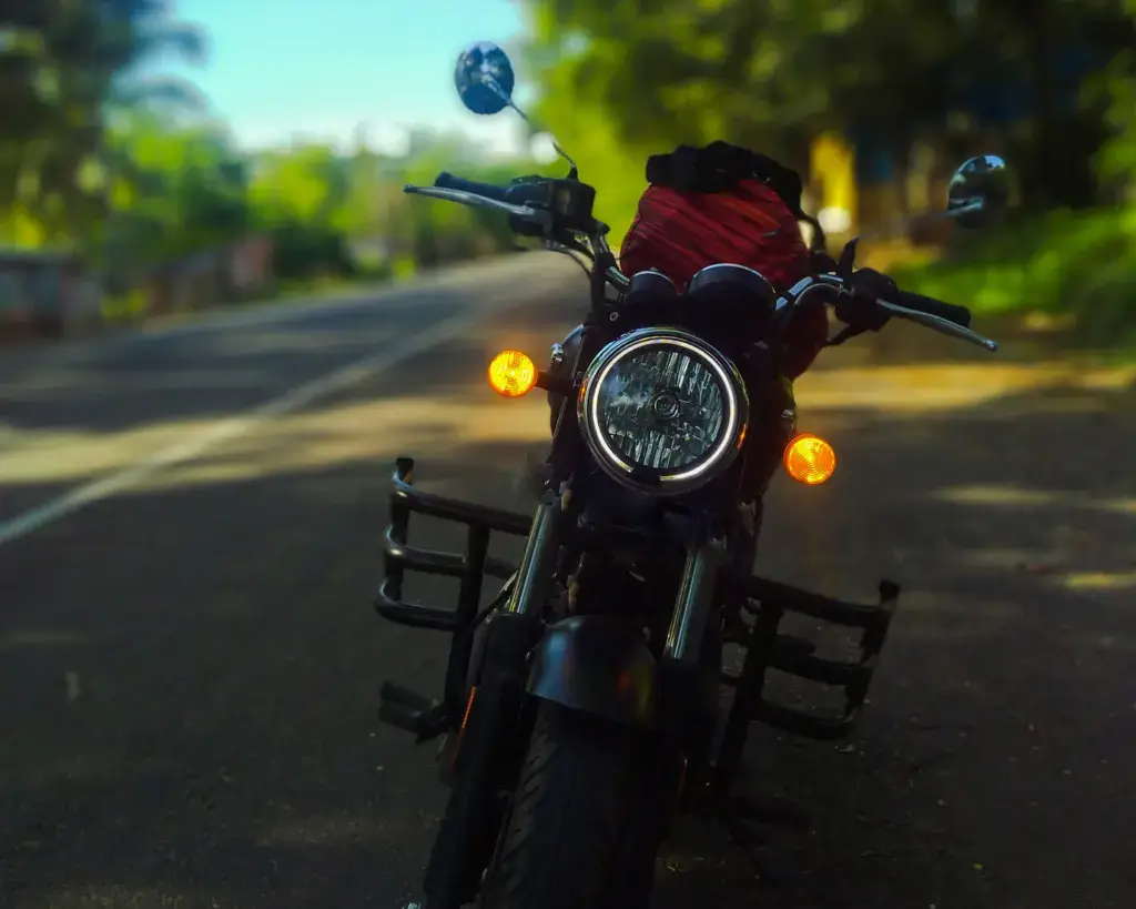 Motorrad mit eingeschaltetem Frontscheinwerfer und Blinkern auf einer Straße mit Bäumen im Hintergrund